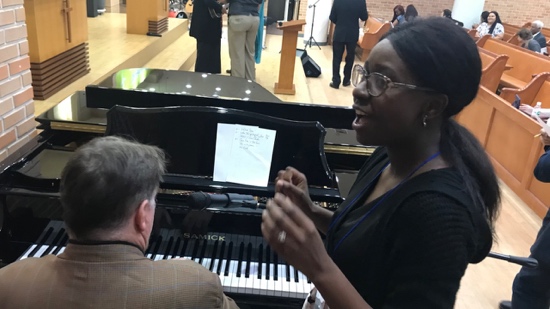 A person standing next to a person playing a piano