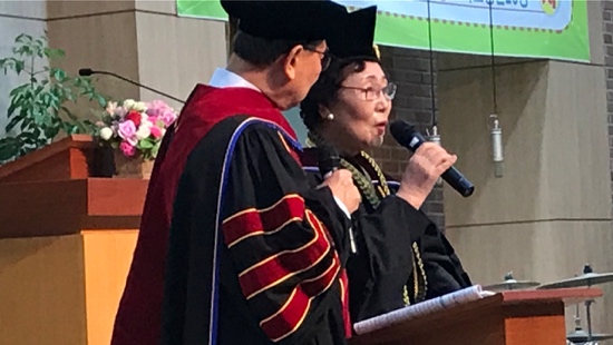 A person and person in graduation gowns speaking into a microphone