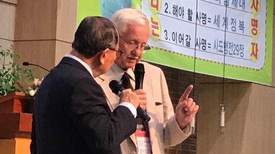 A person in suit holding a microphone and pointing at another person