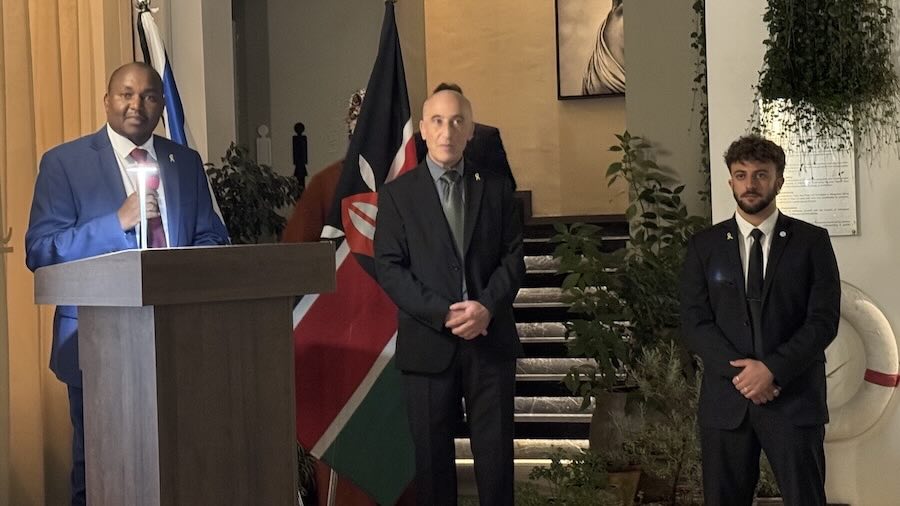 A person in a suit standing in front of a flag