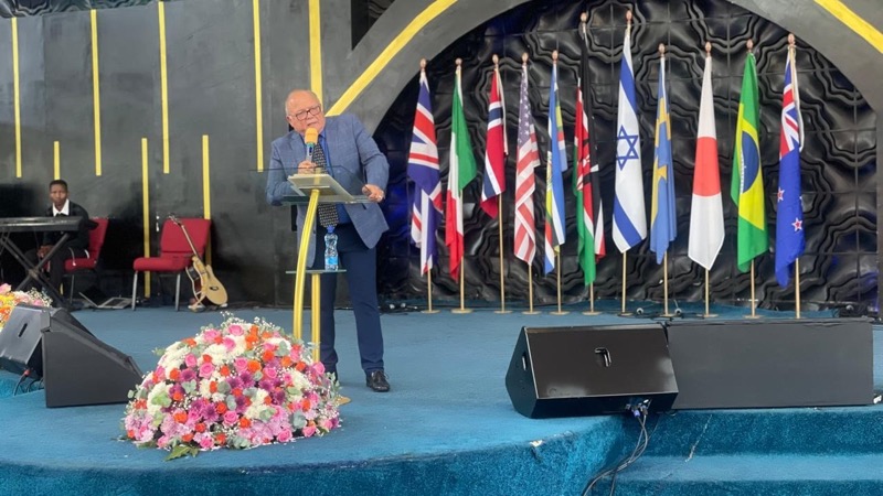 A person standing on a podium with a microphone and flags behind him