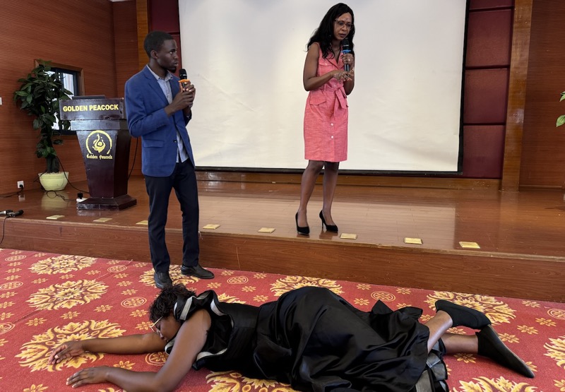 A person lying on the floor with two people holding microphones