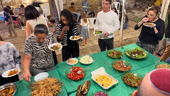 A group of people standing next to a table full of food