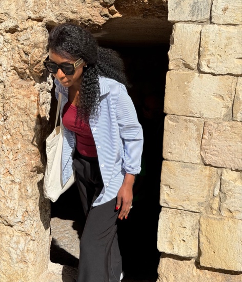 A person in sunglasses and a striped shirt walking through a stone doorway