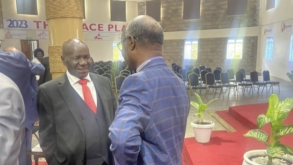 A person in a suit and tie shaking hands with another person in a room with chairs