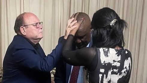 A person holding his head with another person in the background