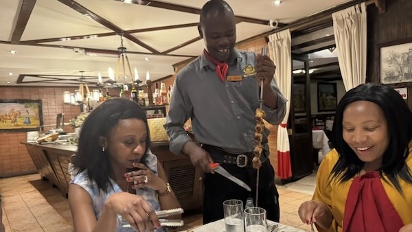 A person holding a skewer and a person sitting at a table