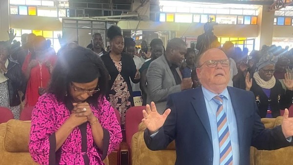 A person and person praying in a room with other people